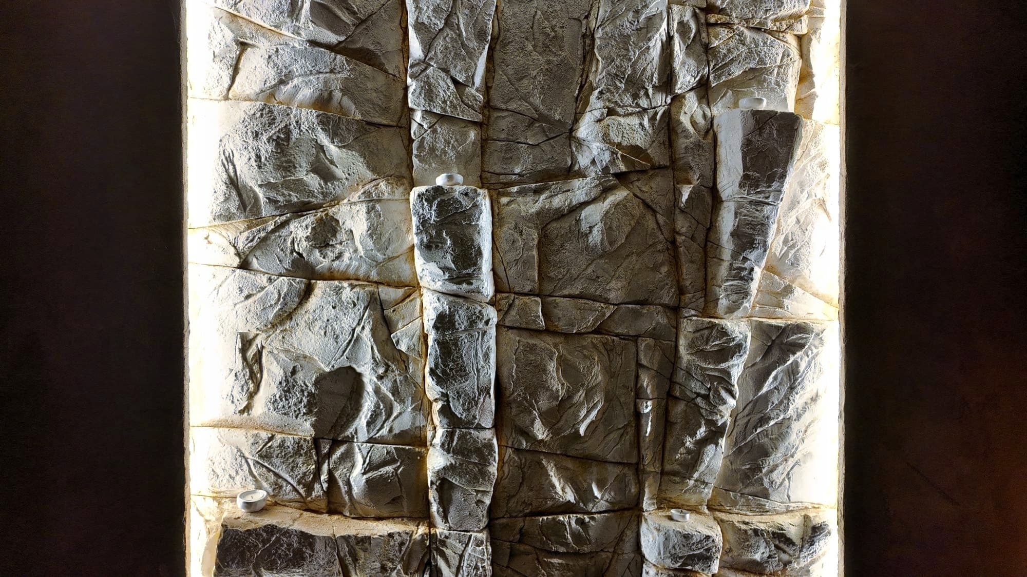 Lähikuva valkoisen kalliopinnan muodoista ja halkeamista, hyllyillä pieniä kynttilöitä