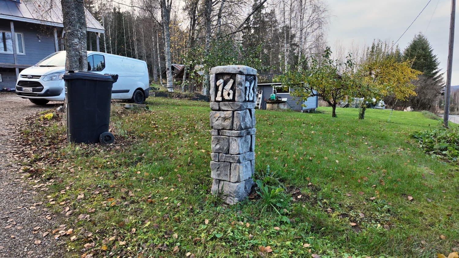Kiviladontaa jäljittelevä portintolppa pihan reunalla, numerot kahdella sivulla