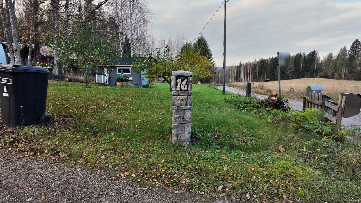 Portintolppa pihatien varressa syksyisellä nurmikolla, taustalla pelto ja metsä